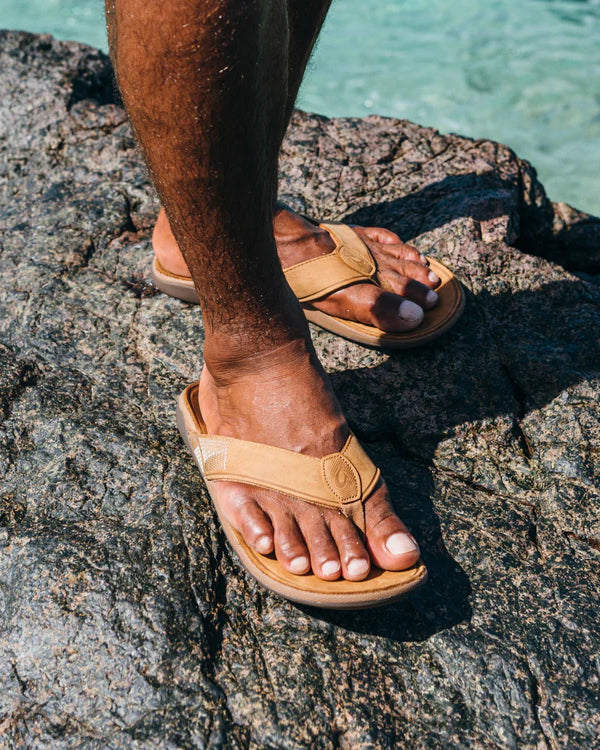 OluKai leather sandals on a rocky shoreline